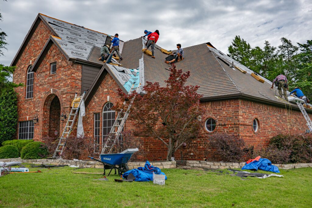 Construction workers repair a brick house roof with ladders and tools on a cloudy day