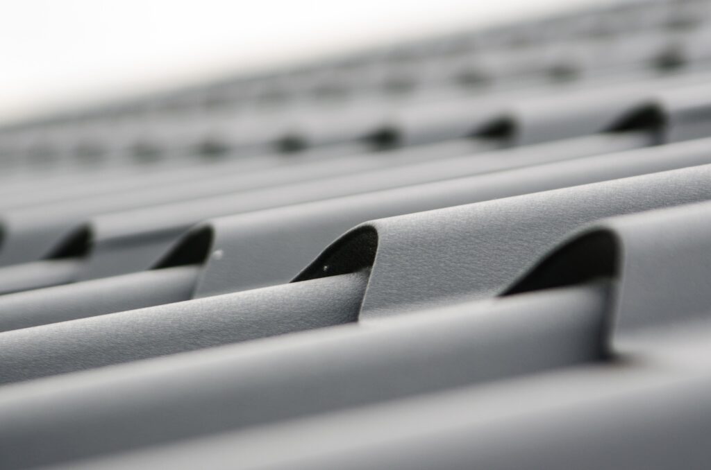 Close-up of a silver metal grate or vent with parallel curved bars and shallow depth of field in the background
