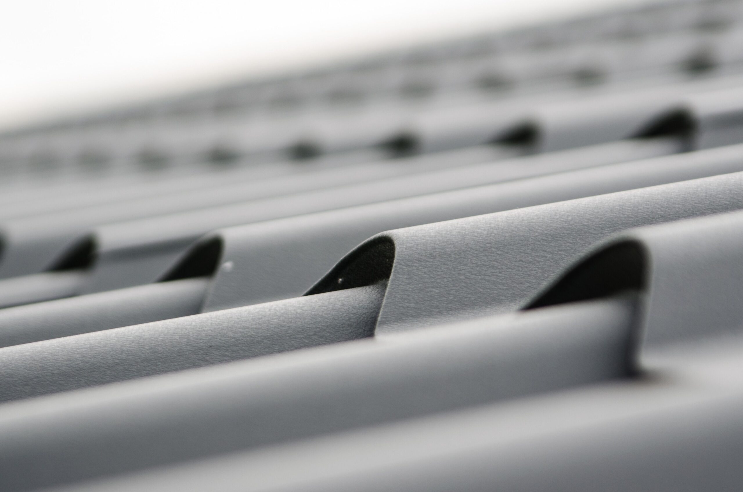 Close-up of a silver metal grate or vent with parallel curved bars and shallow depth of field in the background | scherger roofing