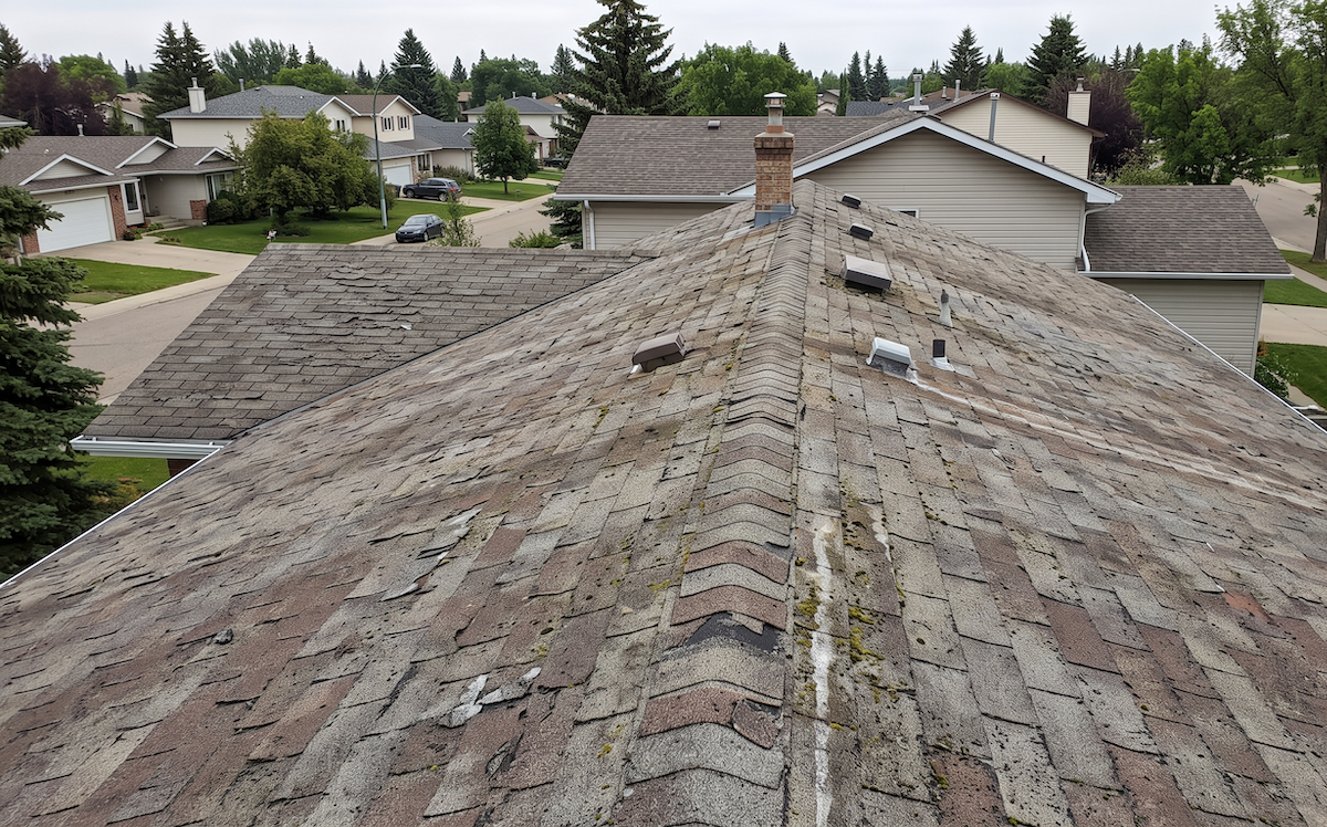 Ageing grey asphalt shingle roof on a suburban home, seen from above