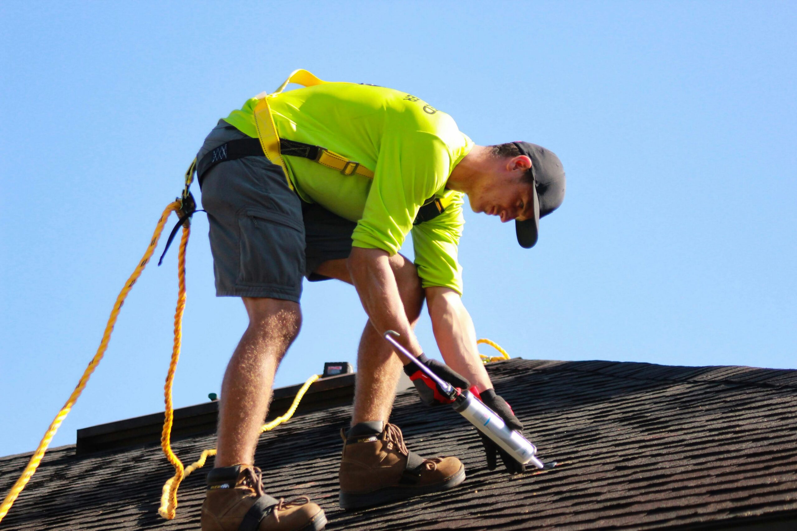 Two workers on a sloped roof wearing safety harnesses and bright ropes under a blue sky. | scherger roofing